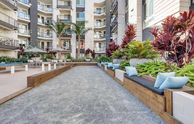A long concrete walkway with a wooden bench on one side and a row of plants on the other.