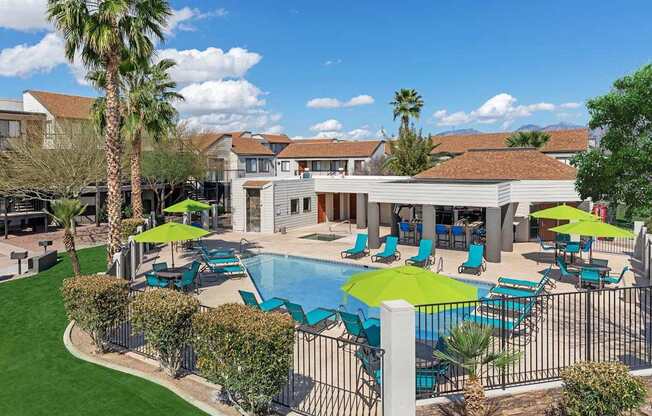 A pool area with a green umbrella and blue chairs.