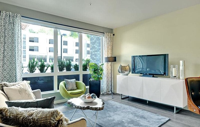 A living room with a white sofa, a green armchair, a glass table, and a television. at Kirkland Crossing Apartments, Kirkland, WA, 98033