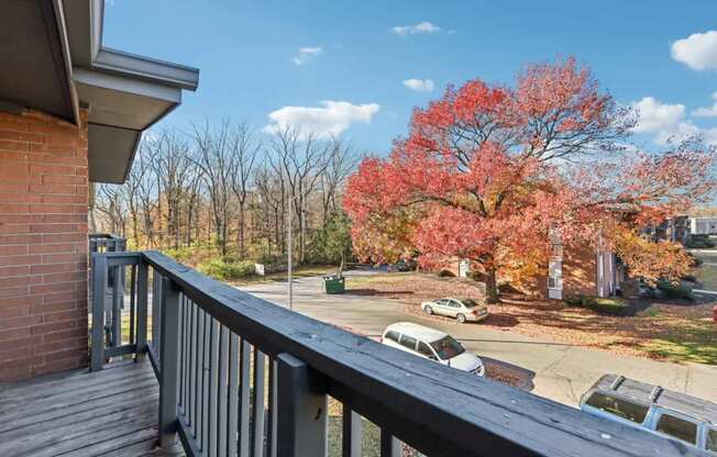 A balcony overlooks a parking lot with cars and trees.