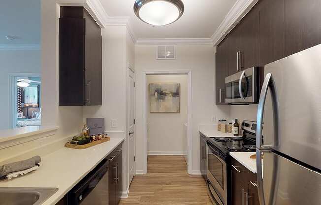 Kitchen with dark cabinets, quartz countertops, vinyl plank floors, stainless steel appliances; open to laundry room