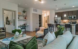 a living room with a couch and a coffee table in front of a kitchen with a counter