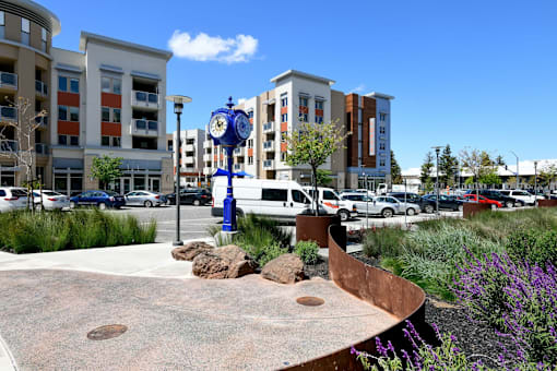 a park bench with a clock in the middle of a parking lot outside Main Street Lofts Cupertino