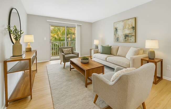 A living room with a grey couch, a grey chair, a wooden table, a lamp, a plant, and a painting on the wall.
