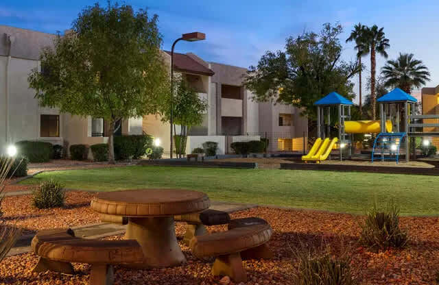 A playground with a slide and a picnic table is lit up at dusk.
