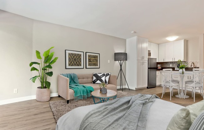 Sleeping and living area of a studio unit with wood-inspired floors throughout, stainless steel kitchen appliances