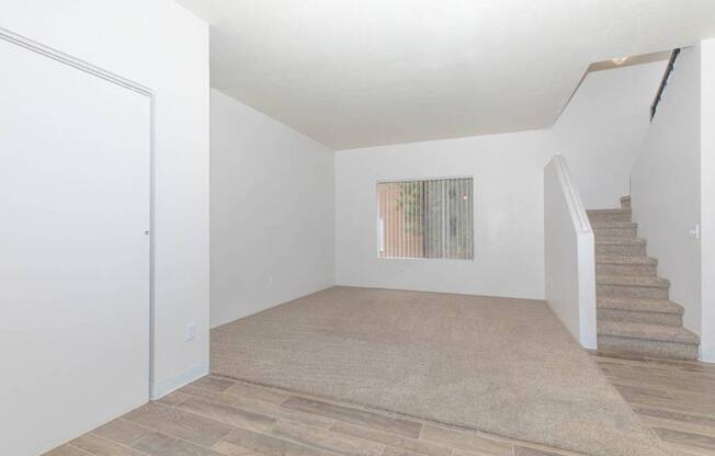A room with a staircase and a window with vertical blinds.