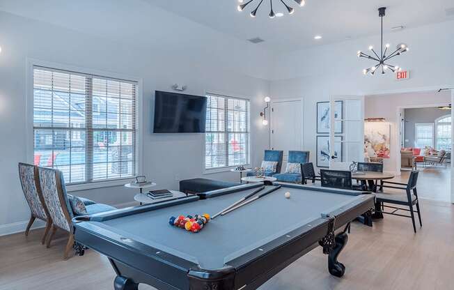 A pool table is in the middle of a room with a television and chairs.