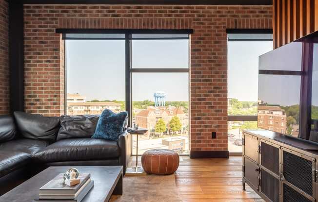 a living room with a black leather couch and a tv and a brick wall