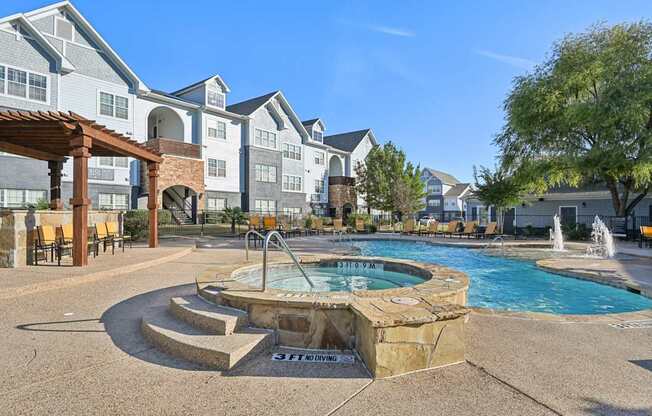 A pool area with a hot tub and a fountain in front of apartment buildings.