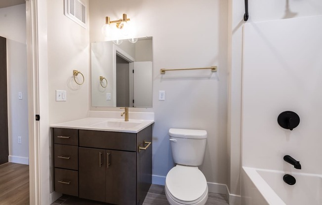 A white toilet sits in a bathroom next to a sink and a bathtub.