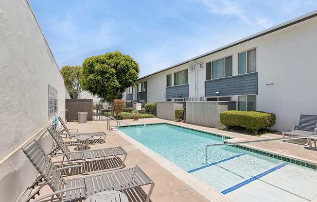 A pool surrounded by lounge chairs and a building in the background.