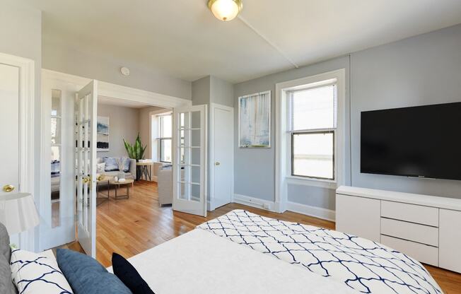 bedroom with bed, dresser, tv, hardwood flooring, french doors, and large windows at the shawmut apartments in washington dc