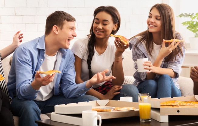 group of young people eating pizza on a couch