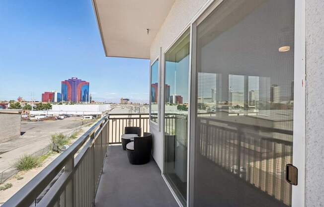A balcony with a black chair and a glass door overlooking a parking lot.