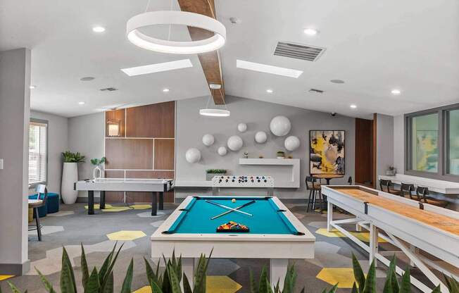 A pool table is in the middle of a room with a shelf and a painting on the wall. at Northpoint Apartments, Tacoma, WA