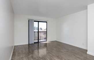 an empty living room with a sliding glass door to a balcony