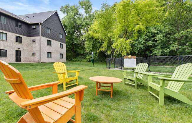 A set of four wooden chairs in different colors are placed on a lawn.