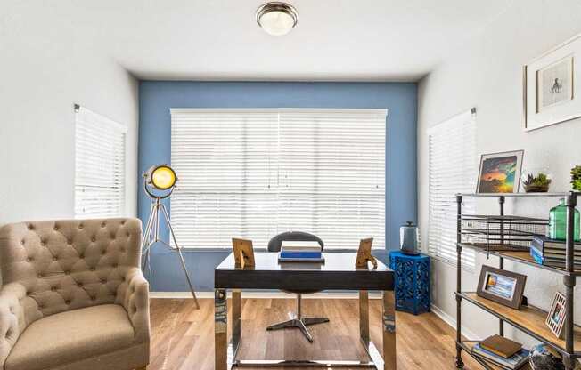 a living room with a blue wall and a window and a desk with a chair