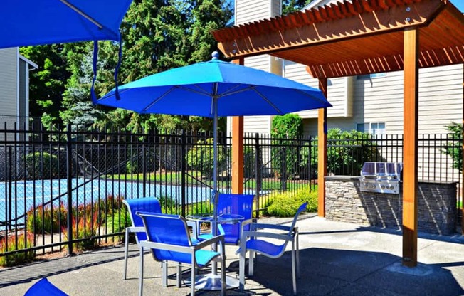 A blue umbrella is on a patio with a pool in the background.