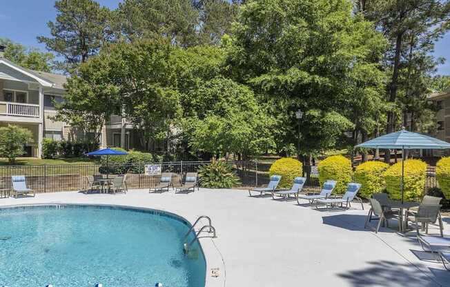 A swimming pool surrounded by trees and chairs.