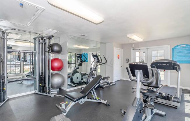 A fitness center featuring cardio machines, weight training equipment, and exercise balls. The space has mirrors on one wall, providing a bright and clean environment for workouts. The overall layout encourages exercise and fitness activities.