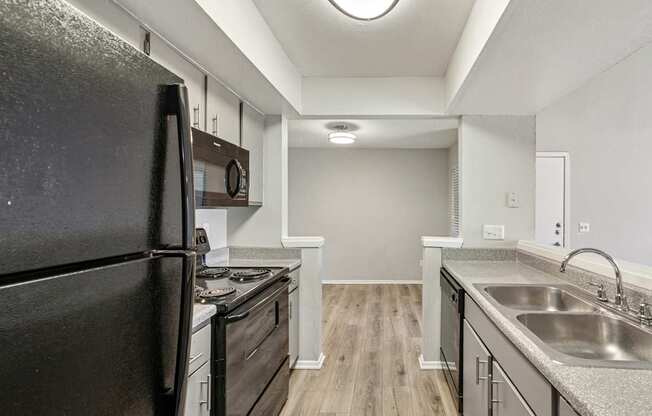 A black refrigerator is in a kitchen with wood floors and stainless steel appliances.