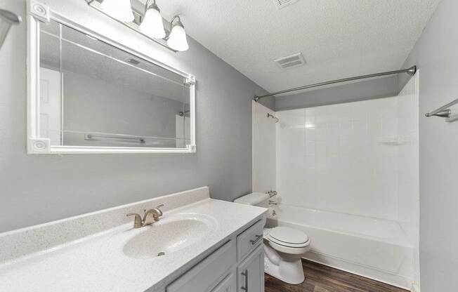 A white bathroom with a sink, mirror, toilet and bathtub.