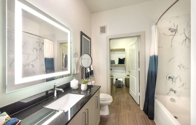 Bathroom area facing sink, back-lit mirror, and bathtub.