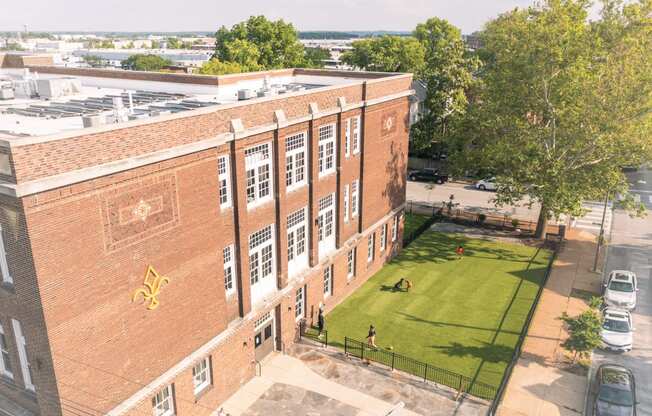 an aerial view of a brick building with a lawn and trees