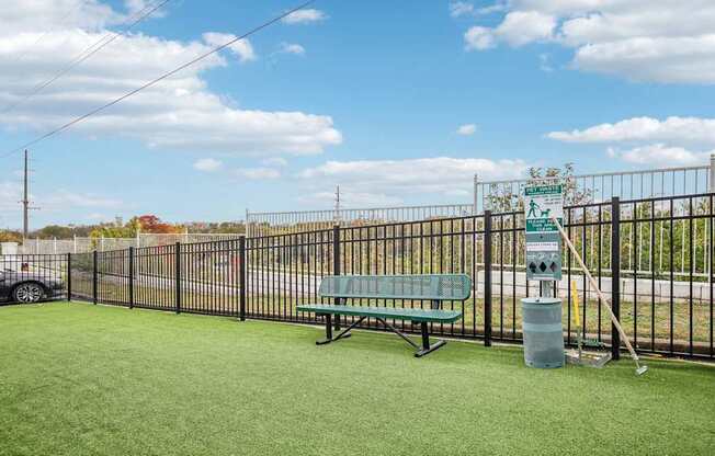 A park with a green bench and a trash can.