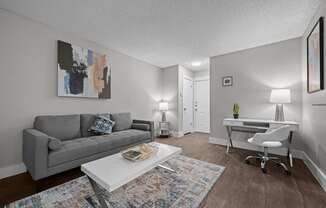 A living room with a grey couch, a white desk, and a painting on the wall.