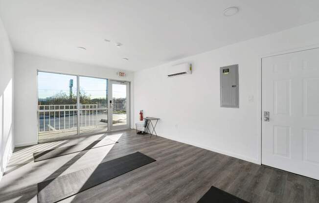 A room with a black rug and wooden floor with a white door and a window.