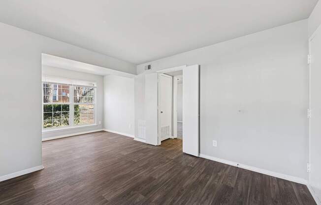 A room with white walls and wood flooring with a doorway leading to another room.