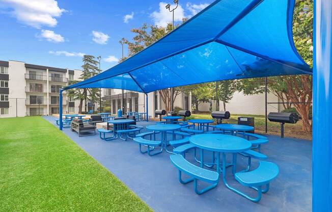 A blue canopy covers a picnic area with tables and benches.