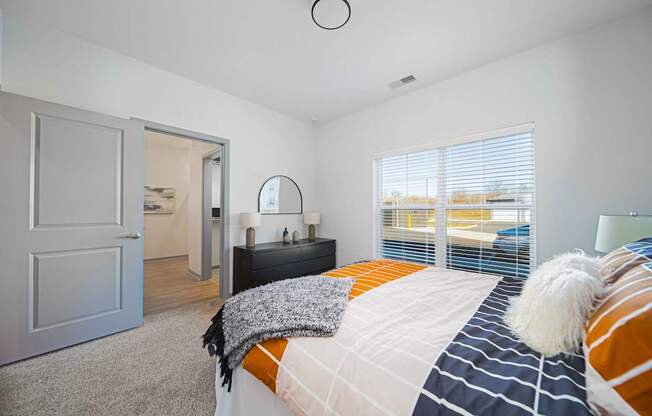 A bedroom with a bed, a nightstand, and a window with blinds.