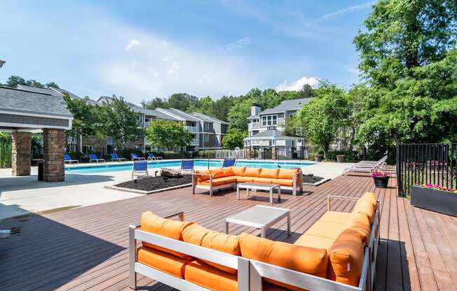 A wooden deck with orange cushions and a pool in the background.