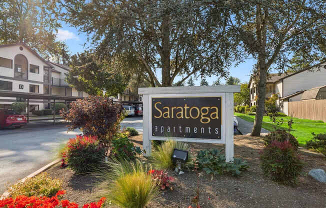 A Saratoga apartments sign is surrounded by flowers and greenery.