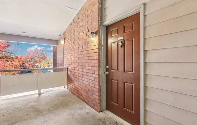 A brown door is on the right side of a room with a brick wall.