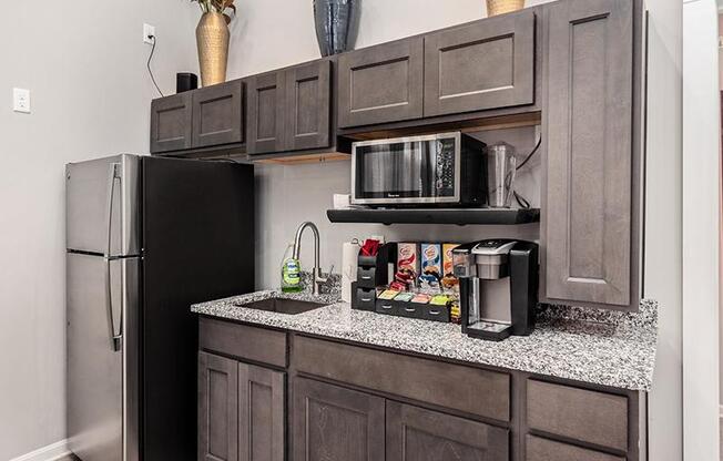 A kitchen with a black refrigerator and a black microwave on a granite countertop.