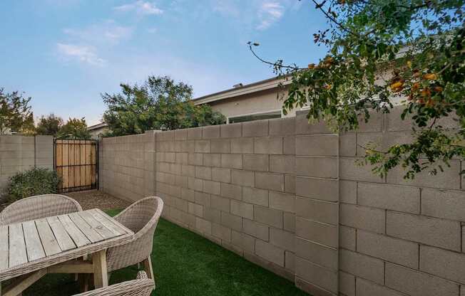 A backyard with a tan wall and a white table and chairs.