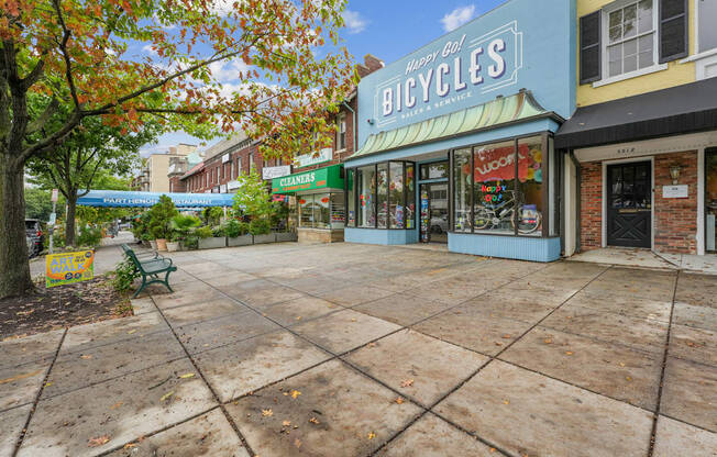 A bicycle shop is located in a plaza with a bench and trees.