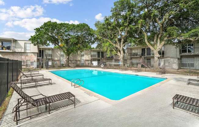 A swimming pool surrounded by trees and lounge chairs in a residential area.