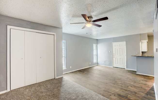 an empty living room with a ceiling fan and a door to the kitchen