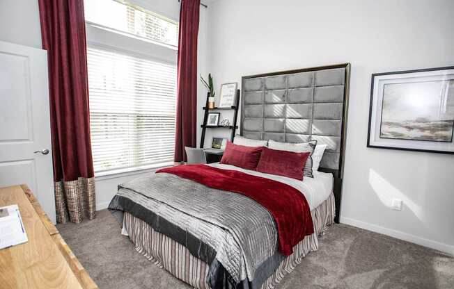 A bedroom with a bed, nightstand, and window with red curtains.