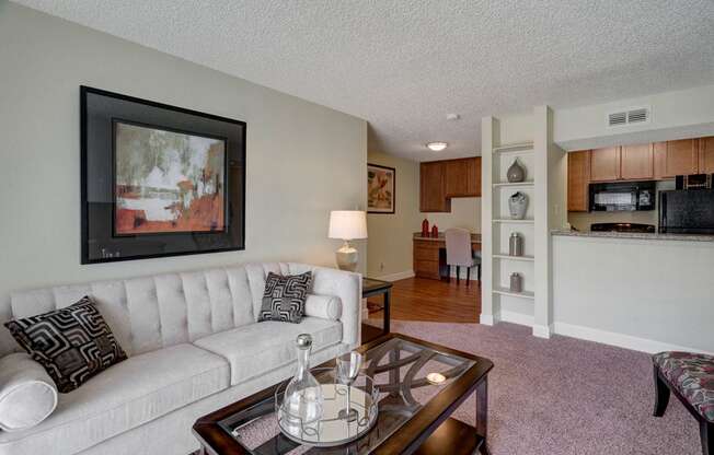 A cozy living area at Acacia Park featuring soft carpeting, a comfortable seating layout, warm accent lighting, and an open connection to the kitchen and dining space for an inviting, easy-to-live-in feel.