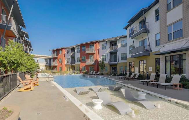A swimming pool surrounded by a concrete patio and lounge chairs at Infinity on the Point Apartments, Dallas 75243