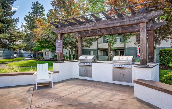 A patio with a grill and a white chair under a pergola.
