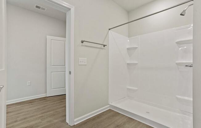A white bathroom with a walk-in shower and a doorway leading to another room.