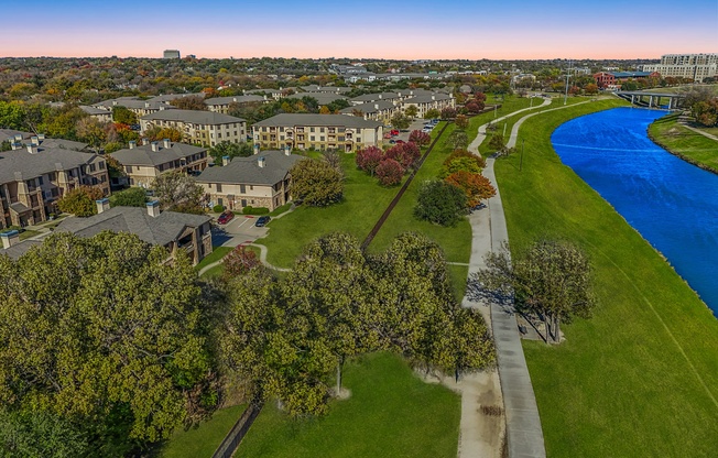 A river flows through a green park with apartment buildings in the background.